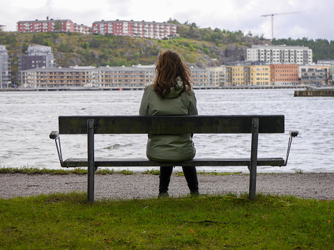 Rear view of woman sitting on bench by river against sky