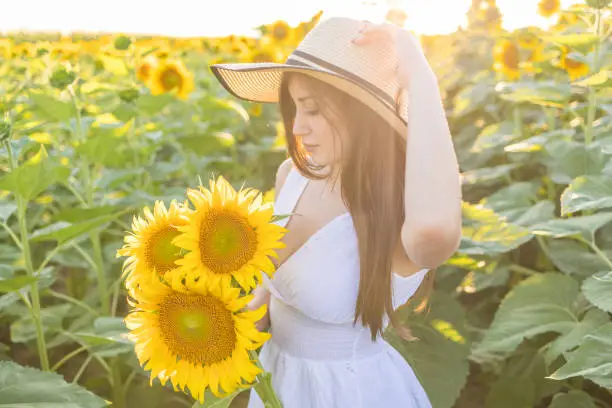 Photo of Girl of natural beauty with a straw hat on her head holds a bouquet of sunflowers and admiring in the beauty of the sunflower.
