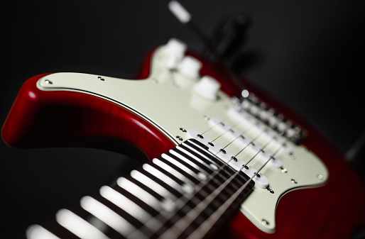 Close-up of a red electric guitar on a black background. Selective narrow focus on pickup.