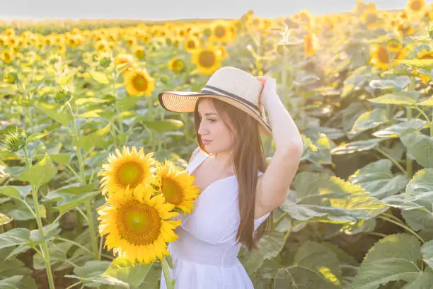 Photo of Girl of natural beauty with a straw hat on her head holds a bouquet of sunflowers and admiring in the beauty of the sunflower.