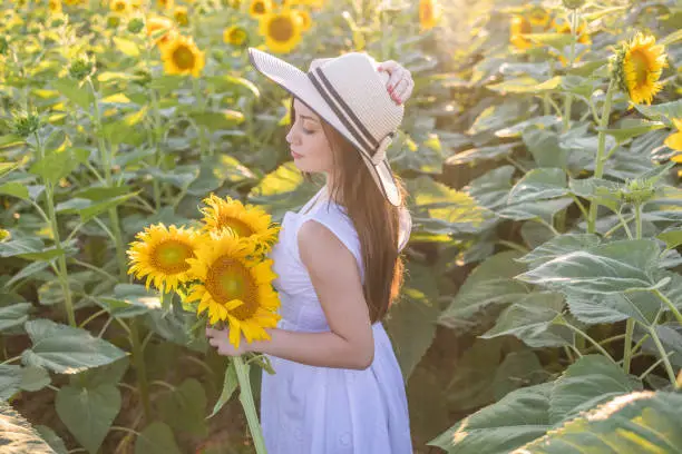 Photo of Girl of natural beauty with a straw hat on her head holds a bouquet of sunflowers and admiring in the beauty of the sunflower.