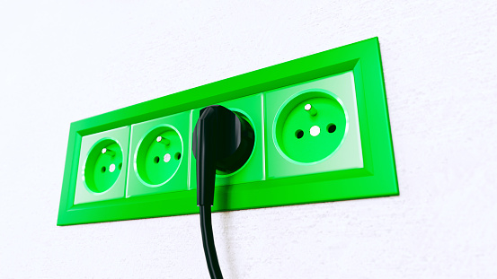 Power socket in wall with a green color. A cable is connected to the socket and a product is using electricity. Concept of a sustainable lifestyle where you use electricity responsible from renewable energy sources.