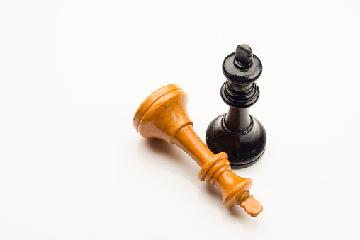 Conceptual image with two pieces of chess board game made of wood on white background . The white king is down and the Black King is standing up.