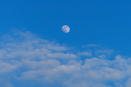 Luminous Moon during the day against the blue sky with cumulus clouds