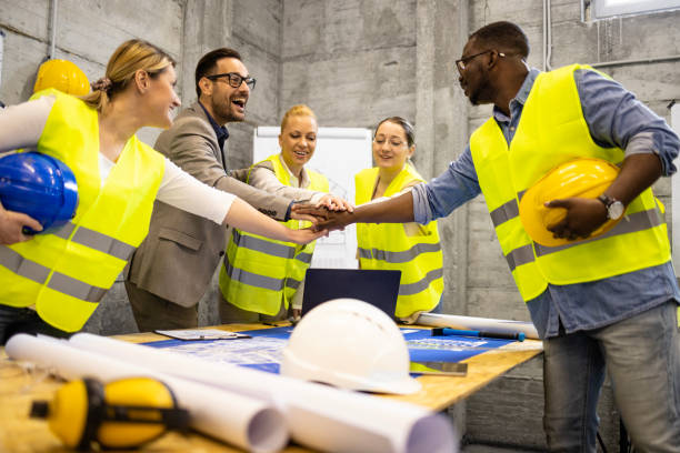 istock Group of structural engineers and architects holding hands together above building plans and blueprints at construction site. 1610492609