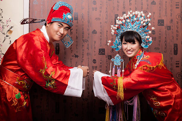Easten Chinese Bride and Groom in traditional wedding ceremony Portrait of Chinese wedding couple in traditional dress in traditional wedding ceremony. The costume is named phoenix coronet xiapei, which is the most typical traditional dress of Chinese wedding. The clothes has hundreds of years history, usually in Chinese red color, it means happiness and good lucky in Chinese culture. They are in process of three bows of ceremony, chinese wedding dress stock pictures, royalty-free photos & images