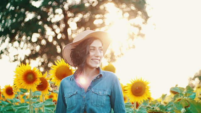 Beautiful young woman wearing a hat and denim shirt in a field with blooming sunflowers
