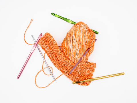 On a white background, there's pumpkin-colored yarn alongside multiple crochet hooks in assorted colors, all isolated.