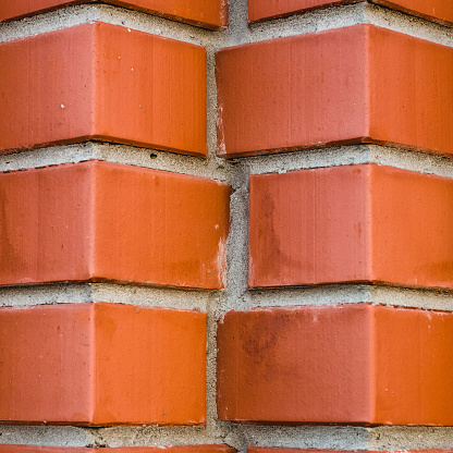 Individual design of red brick wall from diagonally angular bricks close up. Geometric background with brown horn bricks in rows close-up. Minimal backdrop with vivid bricks pattern of original form.