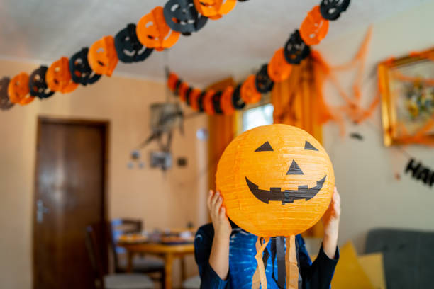 istock A boy is hiding behind a paper pumpkin halloween decoration 1610666990