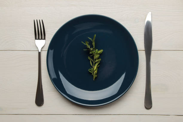 istock Table setting. Blue plate and Cutlery, fork and knife on a white wooden table. top view 1610667150