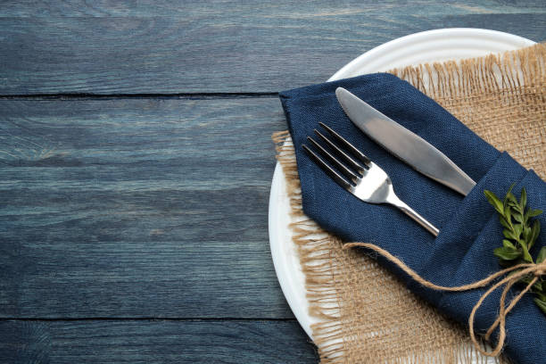 istock Table setting. plate and cutlery in a blue napkin, fork and knife on a blue wooden table. top view 1610667151