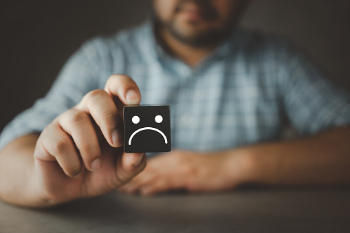 The customer hand picked a sad face icon on the black wood cube. Customer review experience dissatisfied choosing bad rating review Negative idea of unhappy, poor service or poor quality