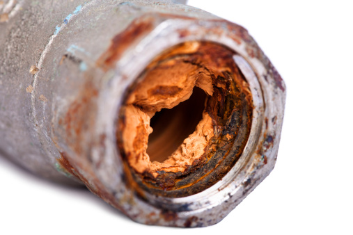 Excerpt of a broken plumbing pipe almost completely blocked with vibrant orange rust. Isolated on white background.