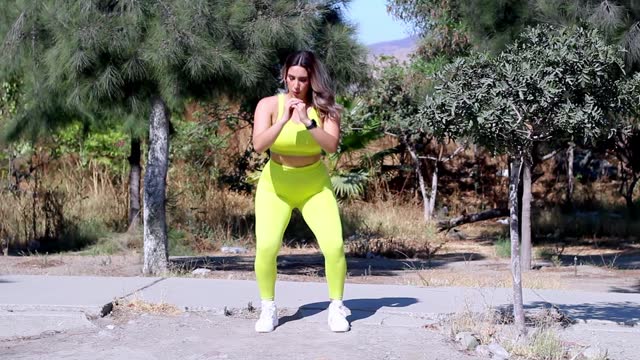 young latin woman athlete training in park doing squats. fitness
