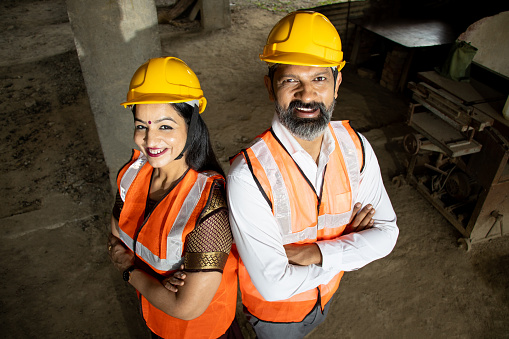 Portrait of two Indian male and female civil engineers or architect wearing helmet standing with cross arms. Real estate. Top angle