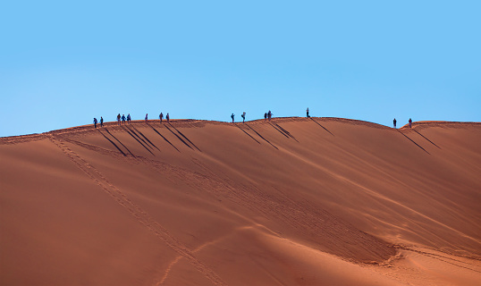 Namibia, Sossuvlei - December 08 2021: Tourists walking up a dune in Sossusvlei - Namib Naukluft National Park, Namib desert, Namibia