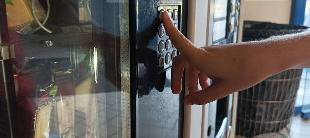 A boy using a modern snack vending machine. His hand touching on vending machine touch screen choosing numbers.