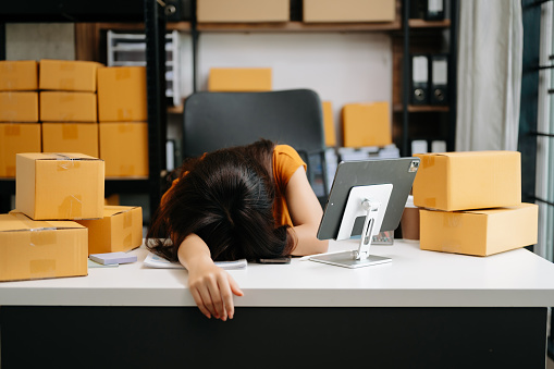 Young Asian owner woman prepare parcel box and standing check online orders for deliver to customer. woman is stressed, bored, and overthinking from working