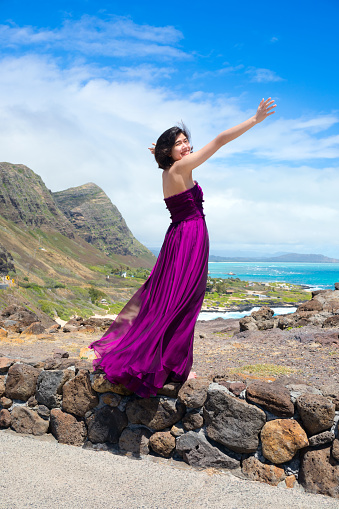 Young woman in formal purple dress standing at Makapu'u Viewpoint overlooking Makapu'u beach and Hawaiian ocean on Oahu, Hawaii