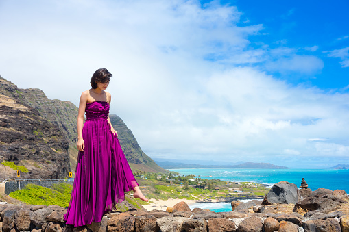 Young woman in formal purple dress standing at Makapu'u Viewpoint overlooking Makapu'u beach and Hawaiian ocean on Oahu, Hawaii