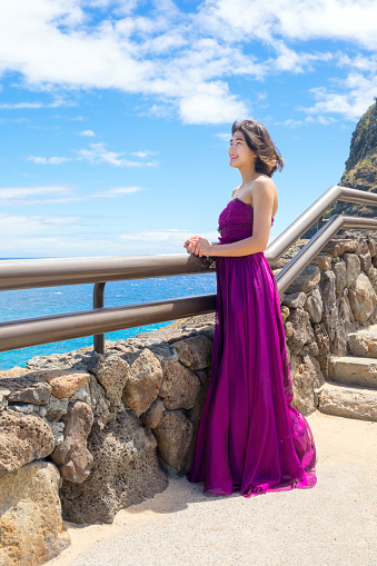Young woman in formal purple dress standing at Makapu'u Viewpoint overlooking Makapu'u beach and Hawaiian ocean on Oahu, Hawaii