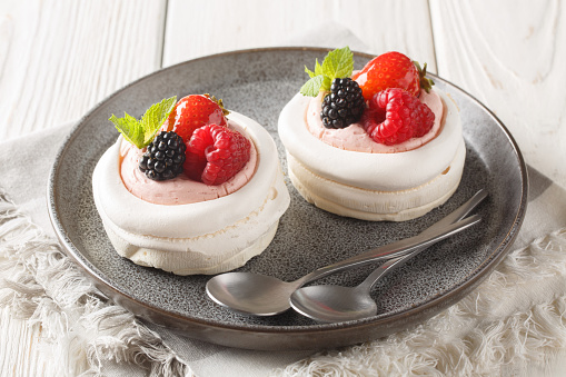 Gourmet Pavlova cakes with fresh berries, cream and mint close-up in a plate on the table. Horizontal