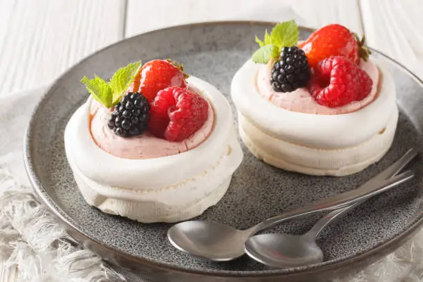 Photo of Anna Pavlova meringue cakes with cream and fresh summer berry closeup on a plate. Horizontal