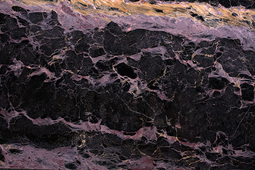 Close-up texture of a black marble formation with pink and orange streaks. The background is a dark, solid color.