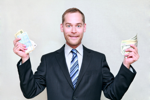 Handsome smiling businessman showing money in his hands, isolated on grey.