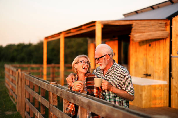 행복한 노부부는 휴가 중이며 오두막 파티오에서 담요와 커피 한 잔으로 따뜻하게 지내며 저녁을 보내고 있습니다. - senior adult retirement mature adult couple 뉴스 사진 이미지