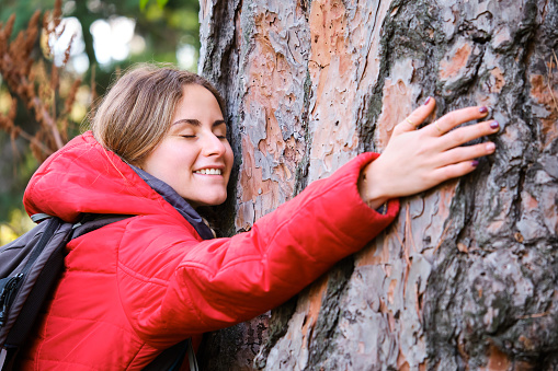 Smiling young female hiker hugging a tree in the forest.