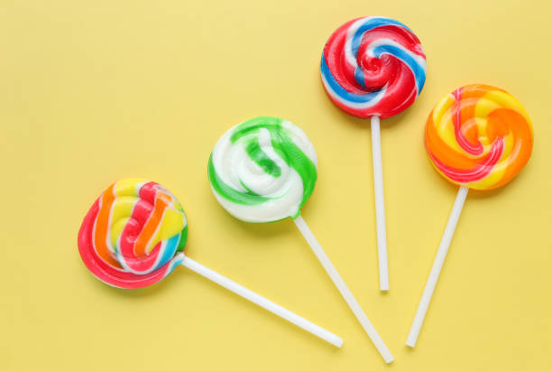 istock Colorful lollipops, different colored round candy on sticks on yellow background. Flat lay, top view 1611399301