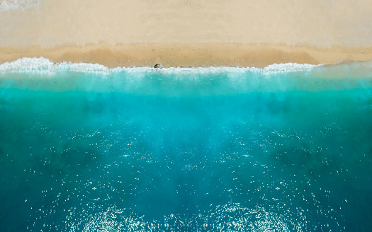 Aerial view of white sand beach coastline and swirling waves with teal blue ocean