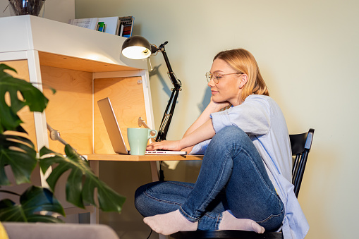 Smiling woman working remotely using laptop from the comfort of her home.