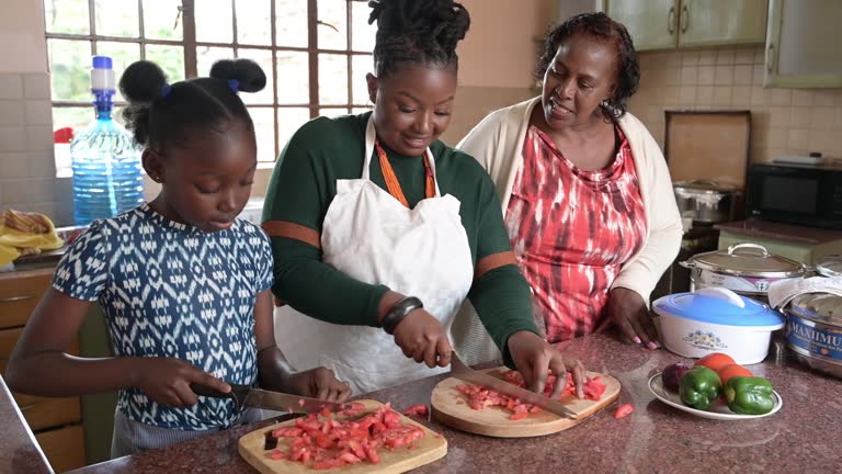 Black women teaching young girl how to slice tomatoes