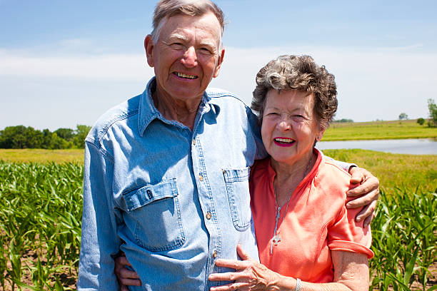 Hardworking Farm Couple Octagenarians Stand the Test of Time A proud hardworking midwestern grandmother and grandfather, farmers, stand proudly together in love, on the family farm. Vast expanse of open fertile land spreads out beyond. Scene  represents "down home" values, hard work, love and Americana at its best. small town photos stock pictures, royalty-free photos & images