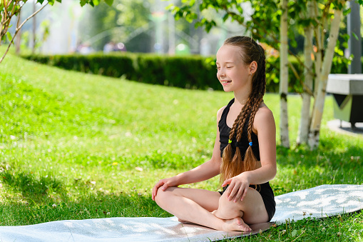 Girl schoolgirl sits in the lotus position in the park. Girl doing meditation sitting cross-legged in the lotus position.