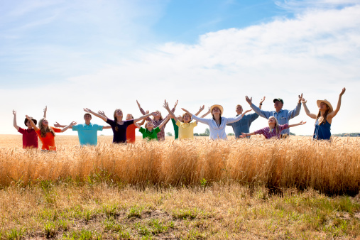 A joyful religious group of family and friends worships God by throwing arms up in surrender, outdoors in a wheat field on a midwestern farm. Could be spiritual image, or alternatively  could symbolize success, inspiration, achievement.