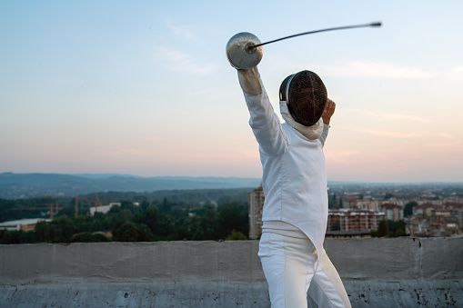 Woman in white fencing costume practicing outdoors. Expensive sport, professional coach, healthy lifestyle.