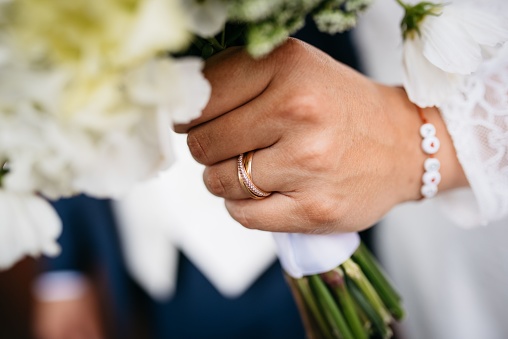 A young adult is holding a bouquet of freshly cut flowers in their hand, with two rings adorning their fingers