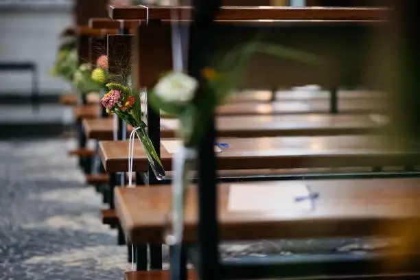 A tranquil scene of a church interior, with two wooden benches in the foreground, each holding a vase of freshly-cut flowers