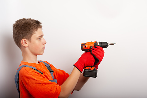 a teenage boy in a work uniform holds an electric drill
