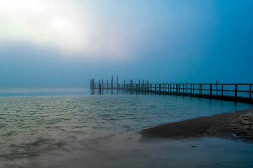 Morning atmosphere at a jetty on the North Sea coast of the island of Föhr with fog and sun slowly fighting its way through the clouds