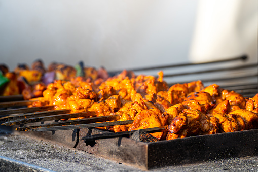 smoking kebab tikka shot with heat haze, smoke coming and butter marinade dripping while a chef cook works in the background showing chicken, mutton food