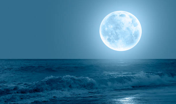 istock Night sky with blue moon in the clouds sea wave in the foreground 1611643902