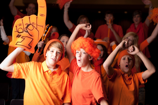 A group of real teenagers and children are enthusiastic sports fans as they cheer at a sports event. Team Color Orange. Shallow DOF. Motion blur. 