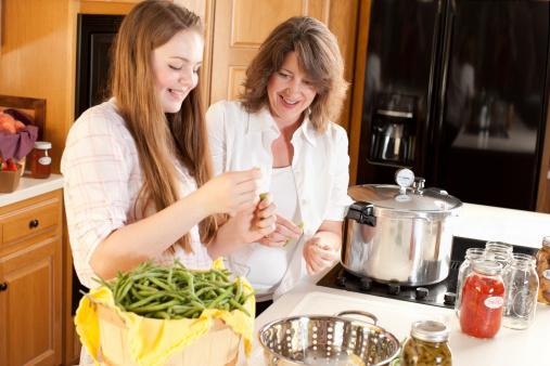 A waist up image of a caucasian mother and teenage daughter canning homegrown vegetables.