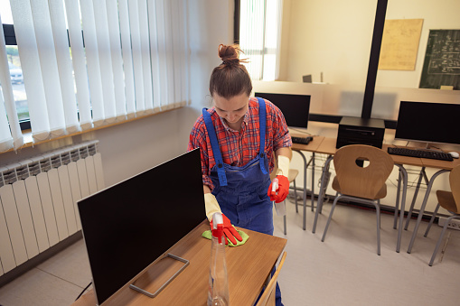 A woman with  gloves cleaning and disinfecting school furniture