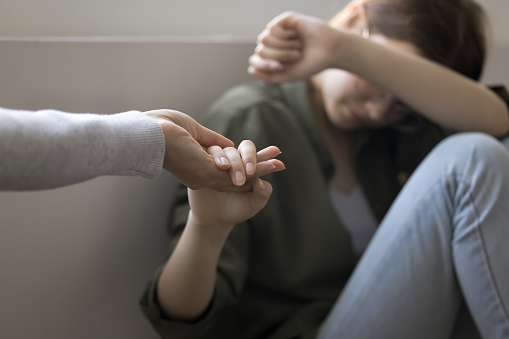 Depressed teenager kid girl taking hand of adult woman, mother, counselor. Psychotherapist giving help, assistance, support to teen child suffering from problems, abuse, difficulties